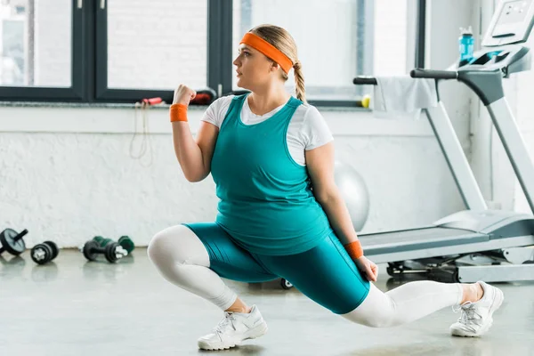 Bella ragazza in sovrappeso in abbigliamento sportivo accovacciato in palestra — Foto stock