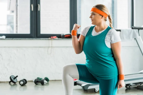 Attraente ragazza in sovrappeso in abbigliamento sportivo accovacciato in palestra — Foto stock