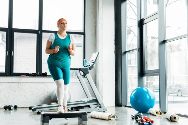 Plus la taille jeune femme faisant de l'exercice sur la plate-forme près tapis de fitness dans la salle de gym — Photo de stock