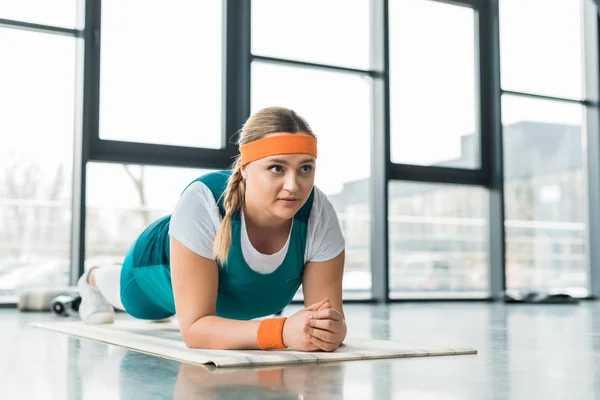 Femme en surpoids faisant de l'exercice de planche sur tapis de fitness — Photo de stock