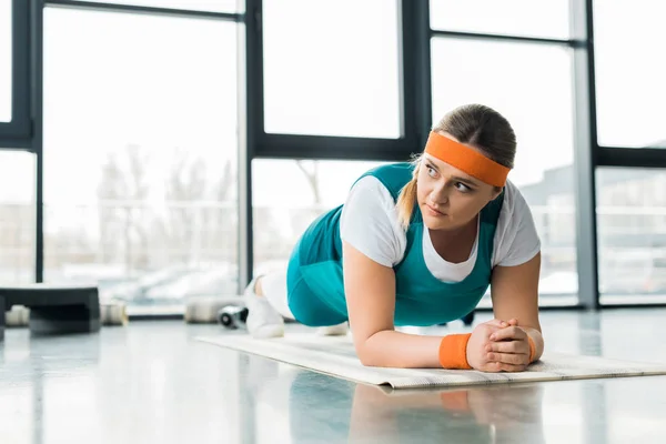 Избыточный вес девушка делает доску упражнения на фитнес мат в тренажерном зале — стоковое фото