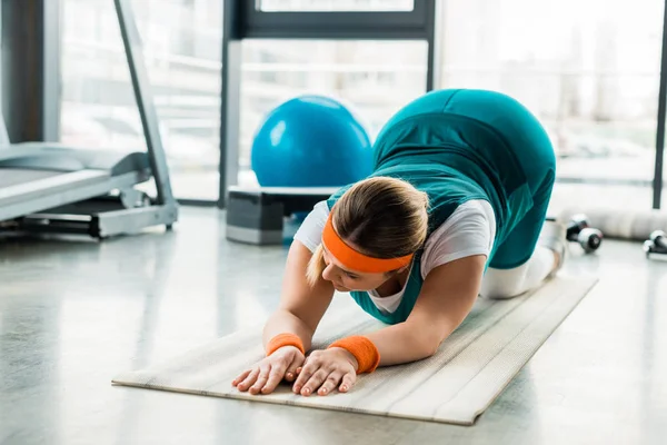 Além de tamanho mulher exercitando no tapete de fitness perto de equipamentos desportivos — Fotografia de Stock