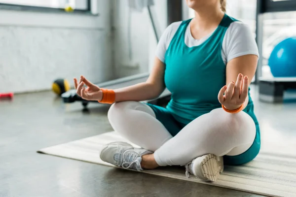 Cropped view of plus size woman sitting on fitness mat with crossed legs — Stock Photo