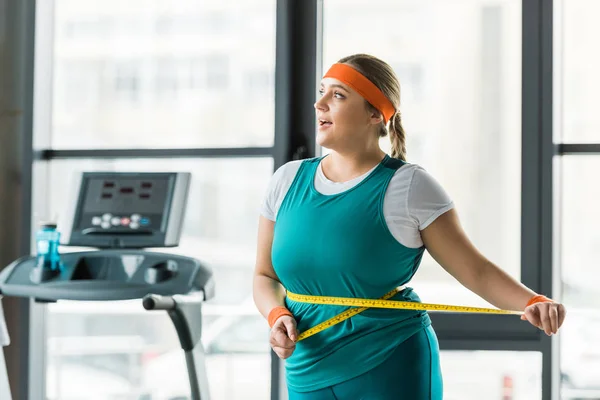 Alegre plus size menina medindo cintura no ginásio — Fotografia de Stock