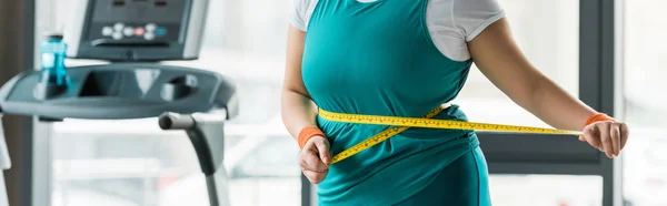 Cropped view of plus size girl measuring waist in gym — Stock Photo