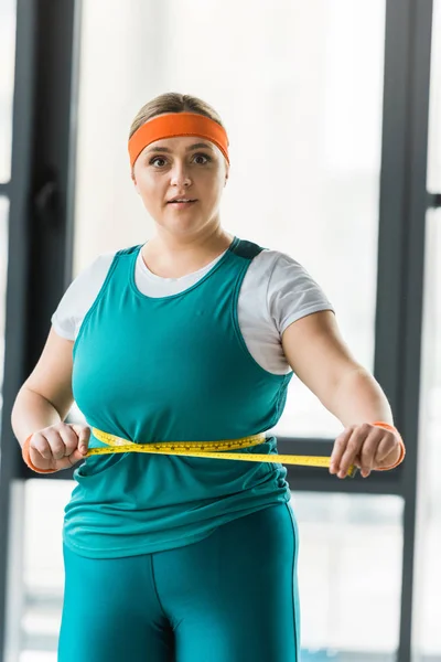 Surprised plus size girl measuring waist in gym — Stock Photo