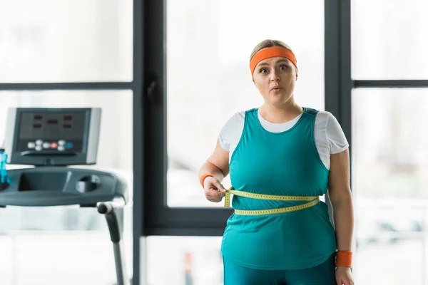Surprised plus size woman measuring waist in gym — Stock Photo