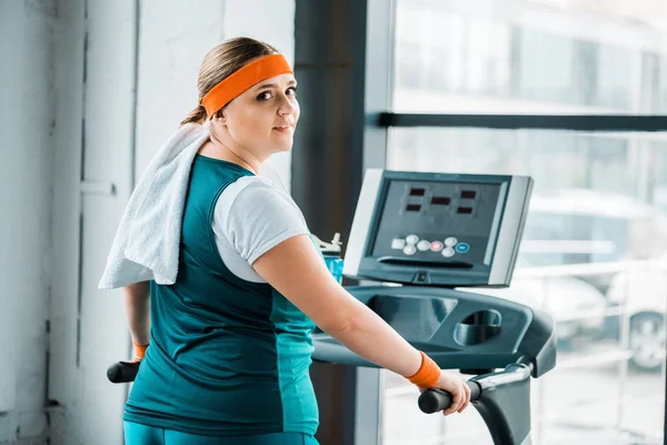 Exhausted overweight girl with towel on shoulders looking at camera on treadmill in gym — Stock Photo