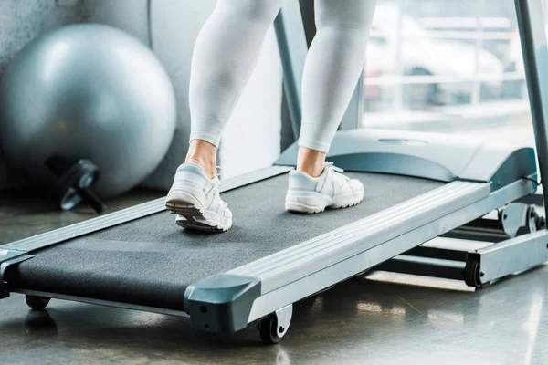 Vue recadrée de plus fille de taille fonctionnant sur tapis roulant dans la salle de gym — Photo de stock