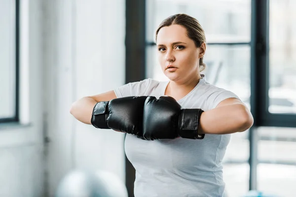 Confident overweight girl standing in boxing gloves while practicing kickboxing — Stock Photo