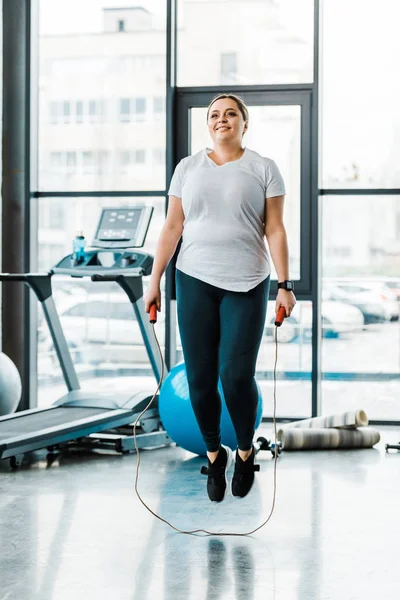 Cheerful plus size woman exercising with jumping rope in gym — Stock Photo
