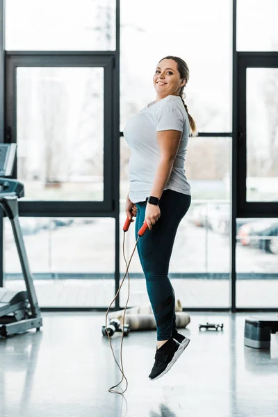 Happy attractive plus size woman exercising with jumping rope in gym — Stock Photo