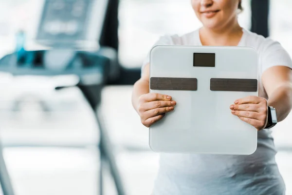 Cropped view of cheerful overweight woman holding scales — Stock Photo