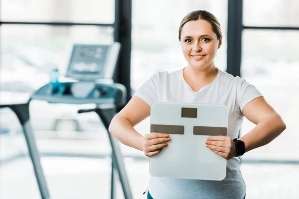 Fröhliche übergewichtige Frau lächelt, während sie Waagen in Händen hält — Stockfoto