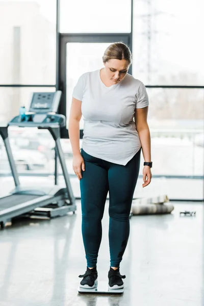 Overweight woman standing on scales in gym — Stock Photo