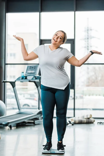 Cheerful overweight woman gesturing while standing on scales — Stock Photo