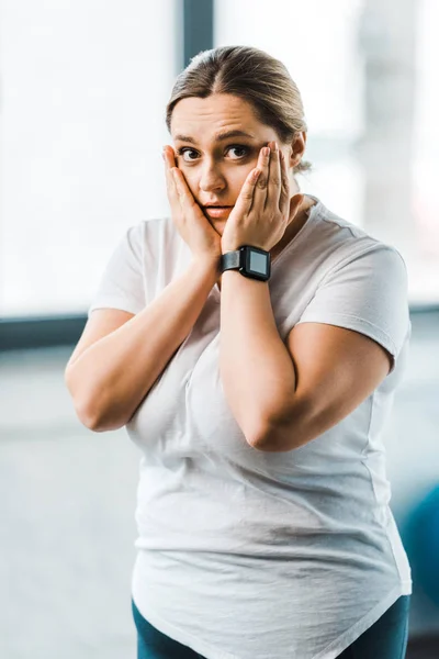 Здивована надмірна вага жінка торкається обличчя в спортзалі — Stock Photo