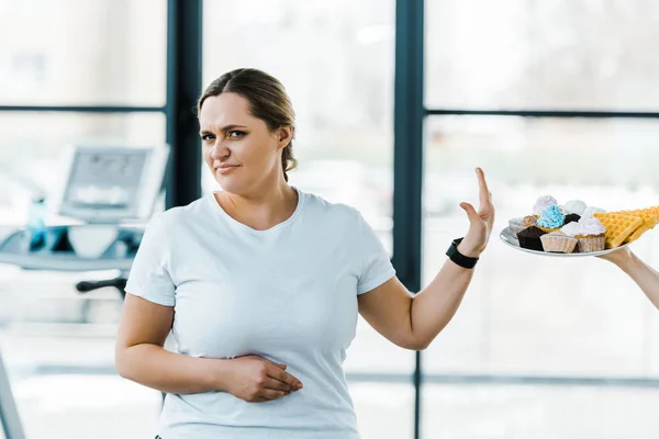 Cropped view of man holding plate with tasty pastry near overweight woman showing no sign — Stock Photo