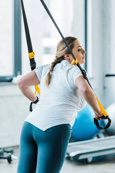 Übergewichtige Mädchen trainieren Arme mit Aufhängebändern im Fitnessstudio — Stockfoto