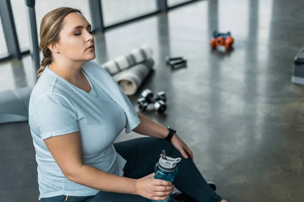 Tired plus size woman resting with closed eyes and holding bottle with water — Stock Photo