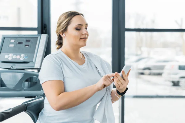 Attractive overweight girl holding smartphone while listening music in earphones — Stock Photo