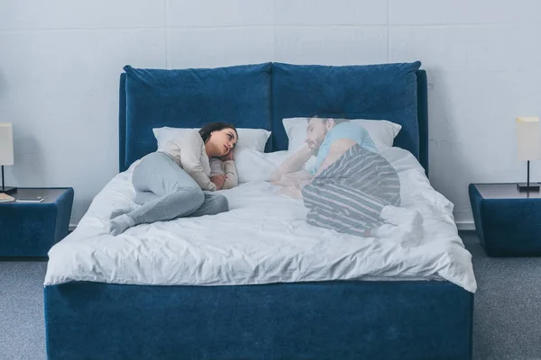 Mujer deprimida acostada en la cama y mirando al fantasma del marido - foto de stock