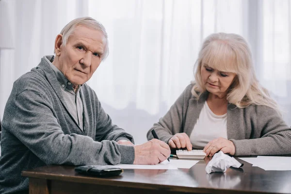 Senior coupe sitting at table with paperwork while counting on calculator at home — Stock Photo