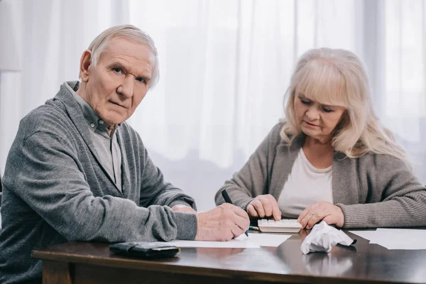 Senior Coupe sitzt mit Papierkram am Tisch und zählt zu Hause auf Taschenrechner — Stockfoto