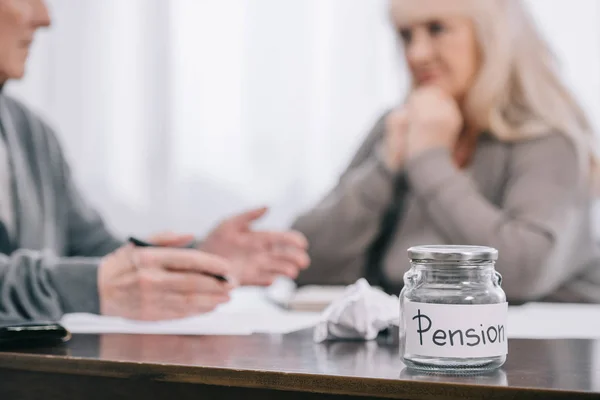 Selective focus of 'pension' word on empty glass jar with senior couple sitting at table on background — Stock Photo