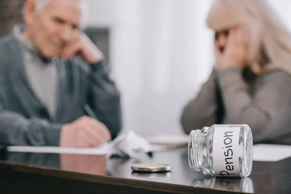Selective focus of 'pension' word on empty glass jar with senior couple sitting at table on background — Stock Photo