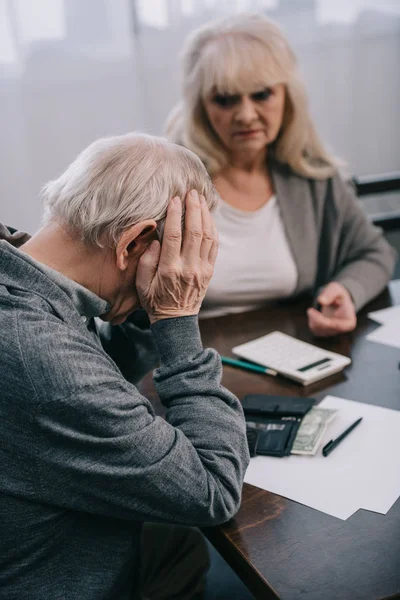 Selective focus of upset senior man with hands on head sitting at table with woman — Stock Photo