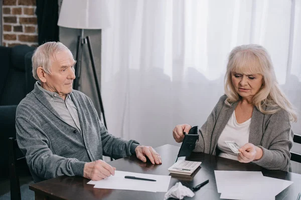 Mulher sênior segurando carteira e dinheiro enquanto sentado à mesa com o homem — Fotografia de Stock