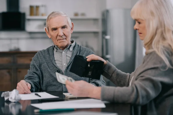 Seniorin hält Geldbörse und Geld bei Tisch mit Mann — Stockfoto