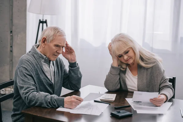 Couple âgé stressé avec les mains sur la tête assis à la table et regardant les projets de loi — Photo de stock