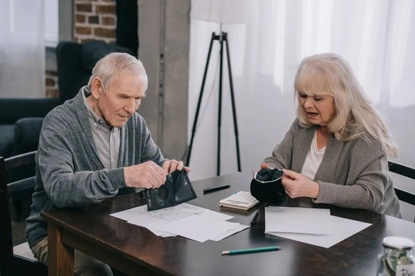 Пожилая пара с бумажниками во время сидения за столом с документами — стоковое фото