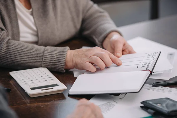 Vista recortada de la mujer mayor señalando con el dedo en el cuaderno con letras ira roth - foto de stock