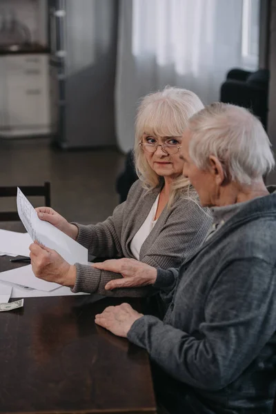 Senior couple in casual clothes holding bills while sitting at table — Stock Photo