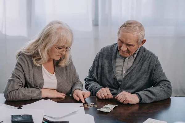 Pareja de ancianos sentados en la mesa con el papeleo, contando dinero en casa - foto de stock