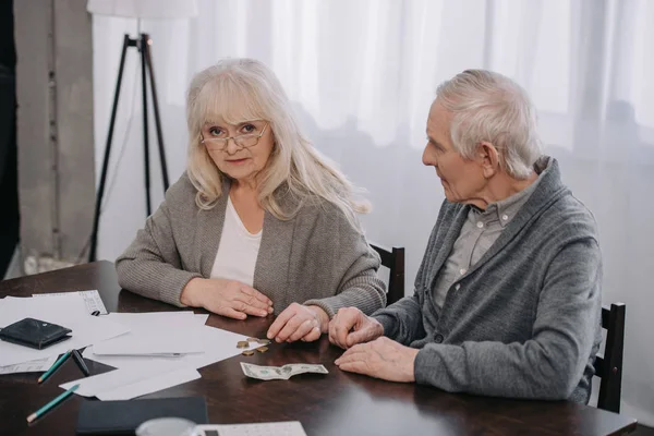 Pareja de ancianos sentados en la mesa con el papeleo, contando dinero - foto de stock