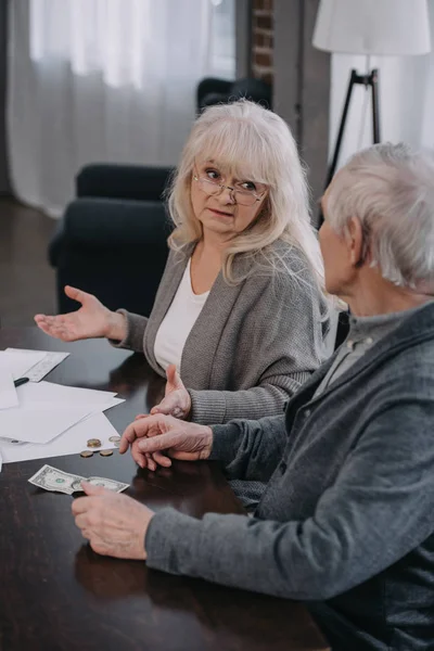 Pareja de ancianos sentados en la mesa con el papeleo, contando dinero - foto de stock