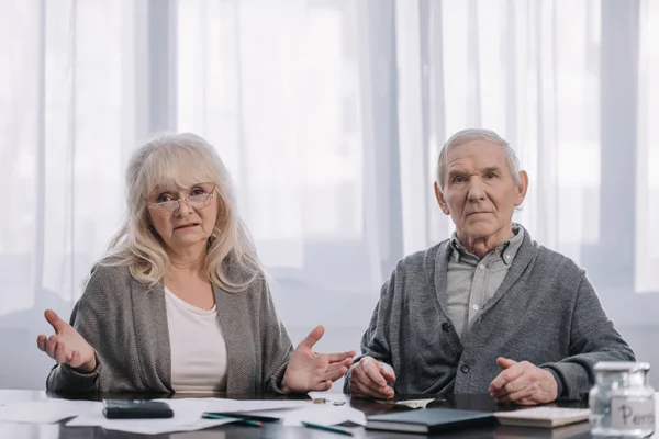 Seniorenpaar sitzt mit Papierkram am Tisch und blickt in die Kamera — Stockfoto