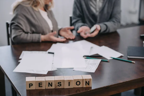 Selective focus of word 'pension' made of wooden blocks with senior couple on background — Stock Photo