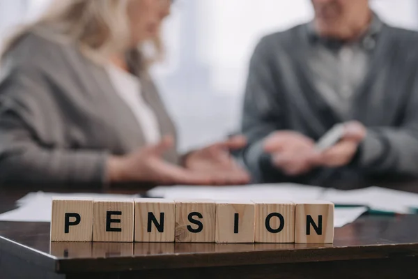 Enfoque selectivo de la palabra 'pensión' hecha de bloques de madera con pareja de personas mayores en el fondo - foto de stock