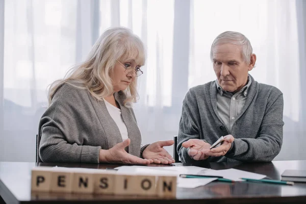 Pareja de ancianos en la mesa con la palabra 'pensión' hecha de bloques de madera en primer plano - foto de stock