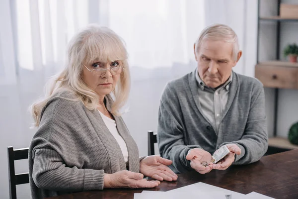 Seniorpaar in legerer Kleidung sitzt am Tisch und hält Geld in den Händen — Stockfoto