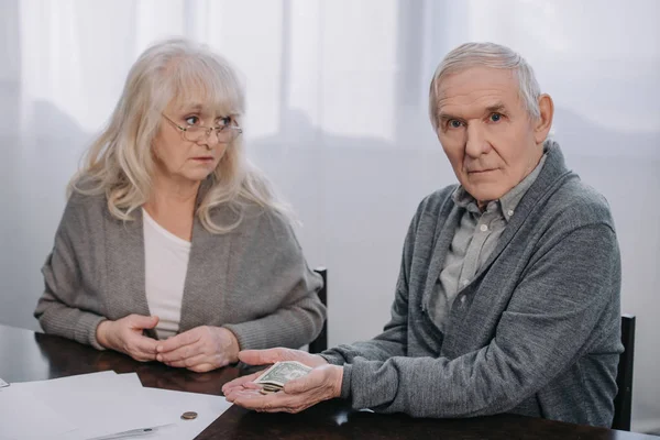 Senior couple in casual clothes sitting at table and holding money in hands — Stock Photo