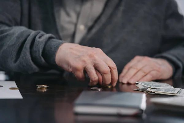 Cropped view of senior man sitting at table and counting money — Stock Photo