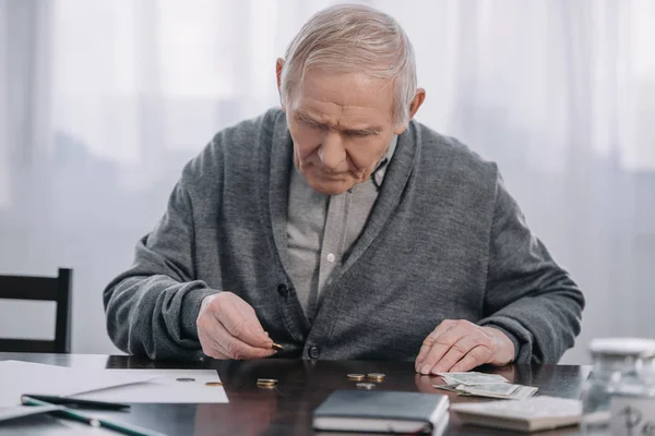 Uomo anziano seduto a tavola e contando i soldi a casa — Foto stock