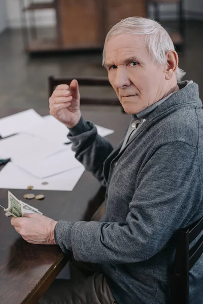 Senior man sitting at table with paperwork, looking at camera and holding money — Stock Photo