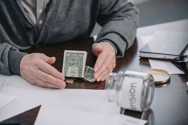 Vista parcial del hombre mayor sentado en la mesa y contando dinero en casa - foto de stock